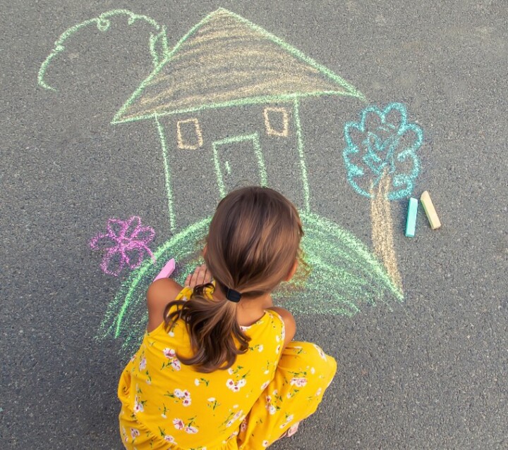 Tyttö piirtää liiduilla maahan talon kuvaa