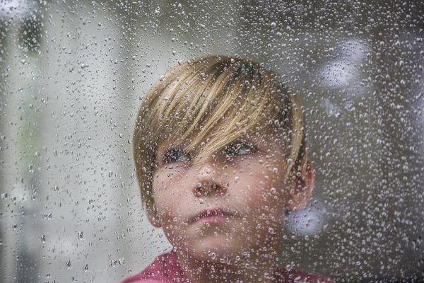 Poika katsoo sateisen ikkunan läpi.